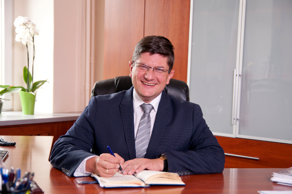 uśmiechnięty prezydent Grzegorz Mackiewicz siedzący przy biurku, wpisujący długopisem informacje do kalendarza